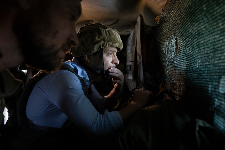Volodymyr Zelenskyy in a military helmet looks out at a front-line position from a shelter in eastern Ukraine