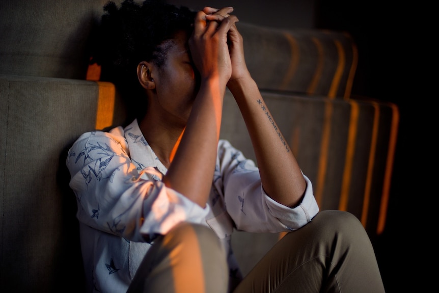 Woman sits down with hands clasped over her face.