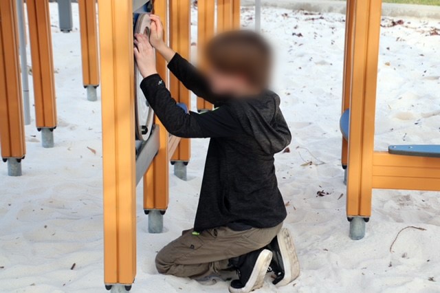 11-year-old crouches in the sand while playing with some equipment at a local park.
