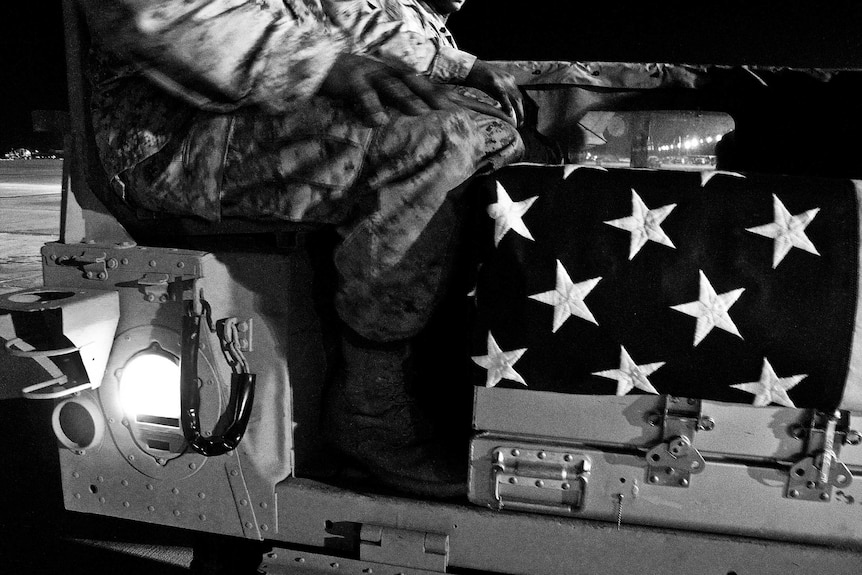 A coffin covered in a US flag sits at the feet of a soldier