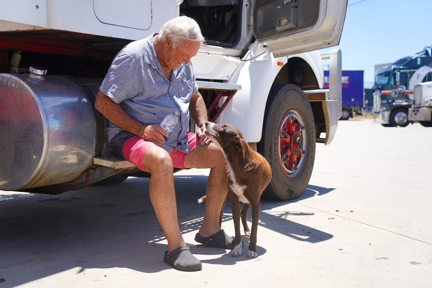 Barry sits on the side of his truck, patting Floss who rests her head on his knee 