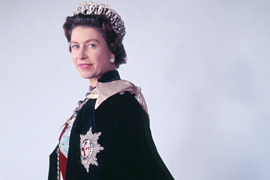 A woman faces side on while wearing a crown and a royal cape.