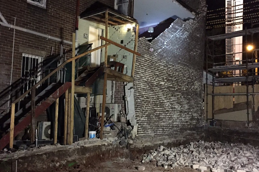 A partially collapsed brick wall at the side of a building