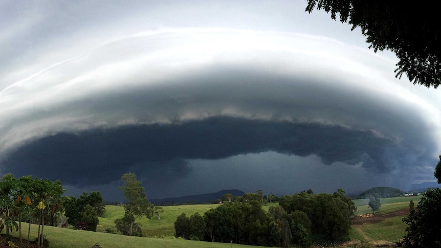 A large, round storm cloud rolls in over hills.