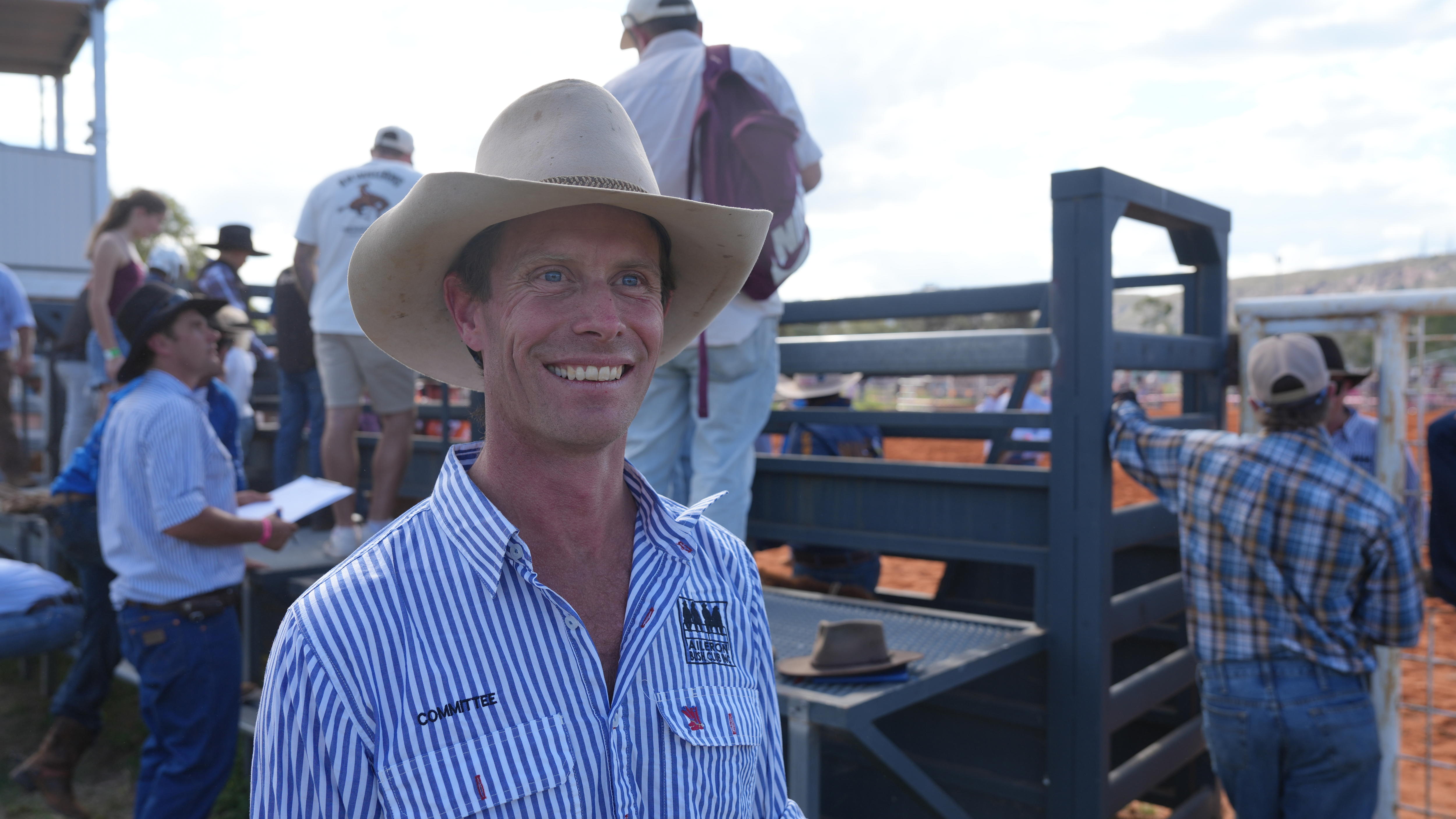 A man in a striped shirt and cowboy hat smiles broadly