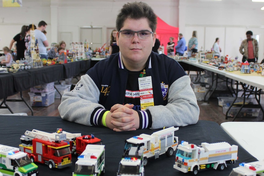 Tristan sitting behind a table of his work. He has his hands clasped.