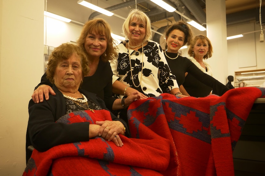 Five women gathered around a red woven blanket