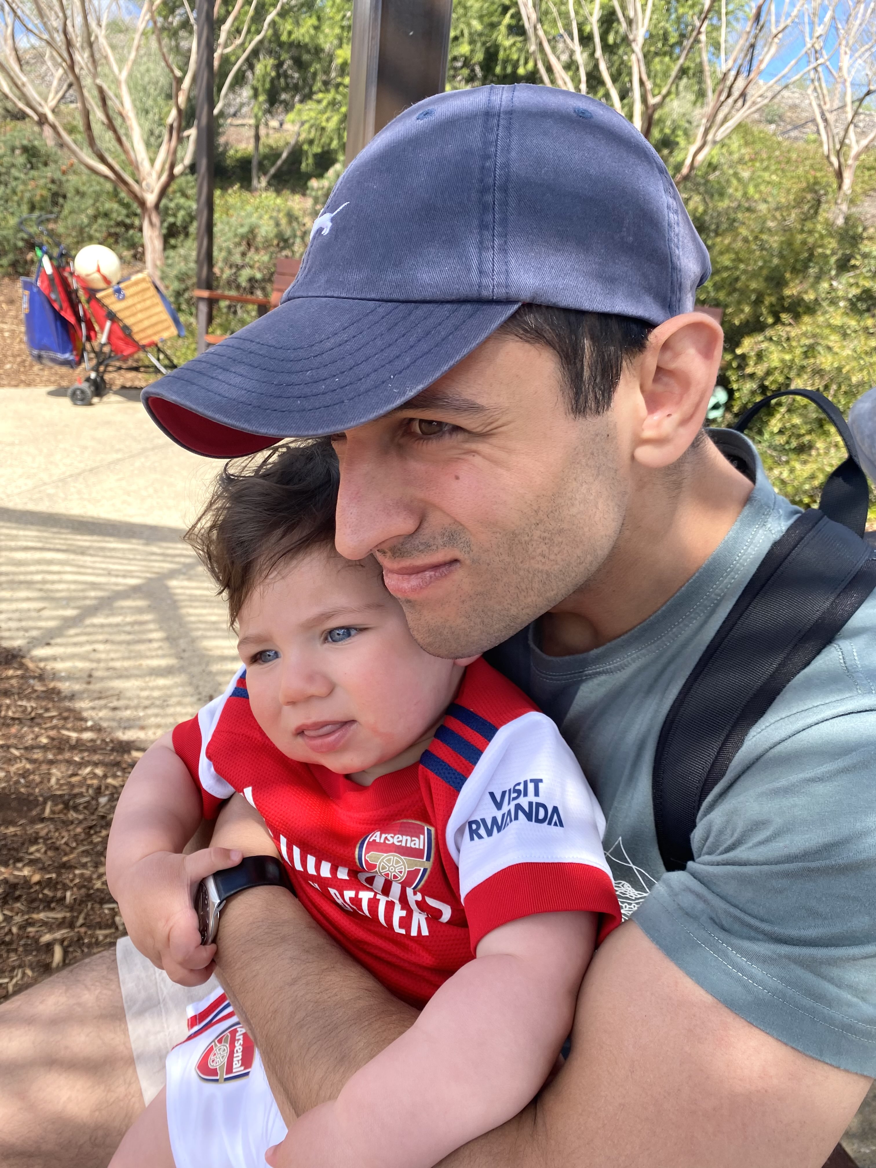 Isaac smiles while holding his young son in his lap. The baby boy is wearing an Arsenal jumper. 