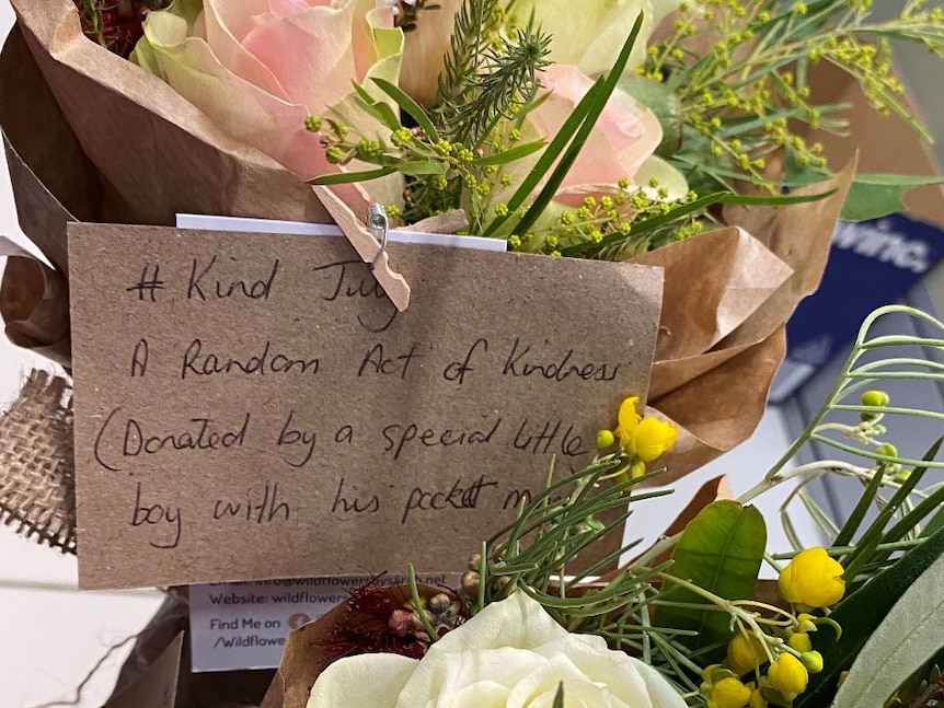 A bouquet of flowers with a note attached, that reads '#Kind July, a random act of kindness 
