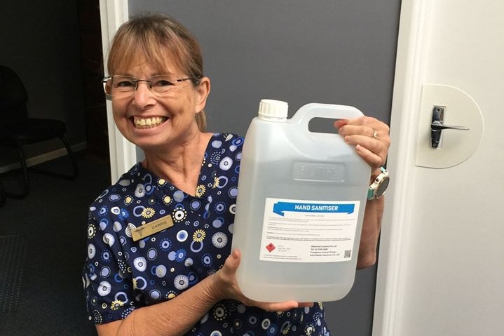 A woman holds up a bottle of hand sanitiser and smiles broadly.