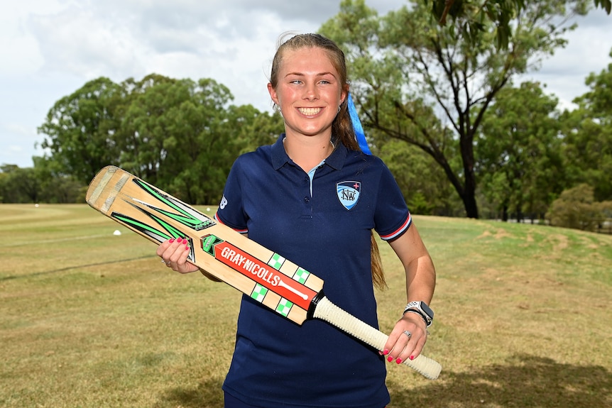 A young woman with a vision impairment stands holding a cricket bat.