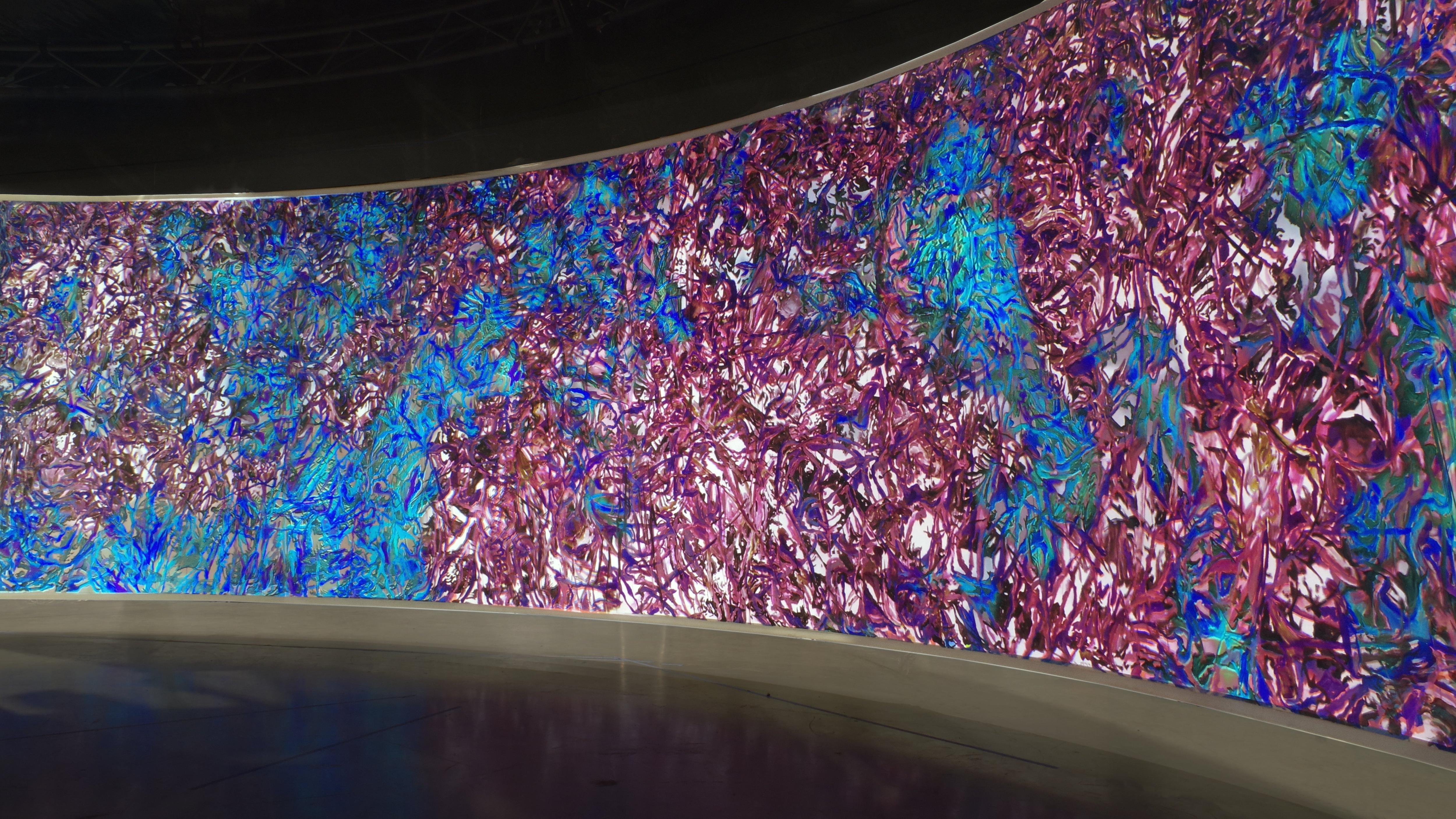 A large, curved video screen, with an intricate, bright pink and blue pattern moving on it.