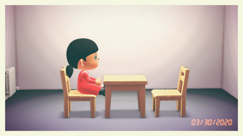 A photo of 3D game character with dark ponytail and red dress sits at wooden table on chair opposite empty chair in empty room.