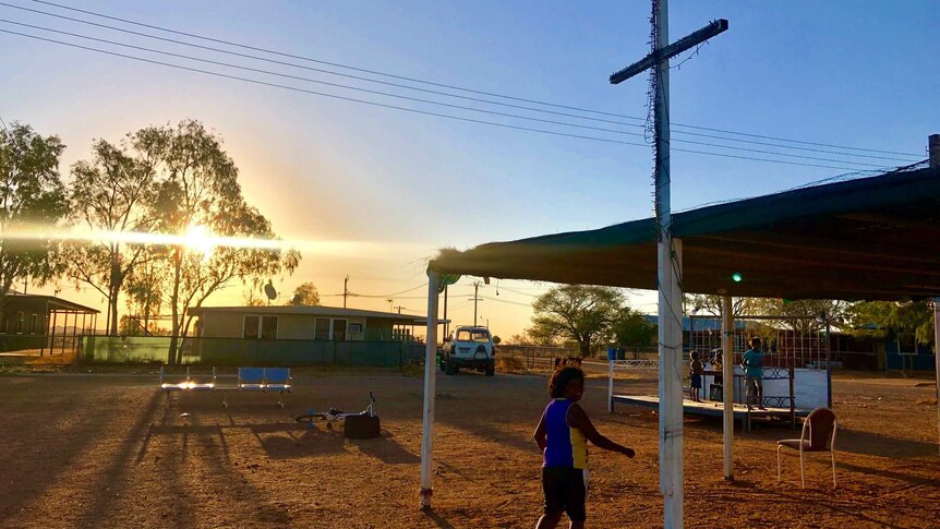 A young Aboriginal boy runs into the sunset under a giant white crucifix with fairy lights