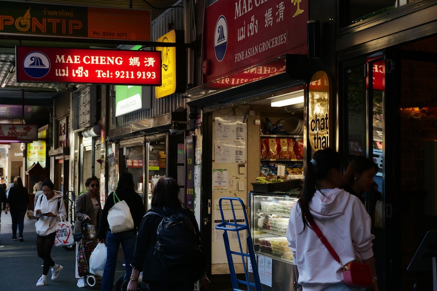 Shoppers walk past stores with signs in English and Thai