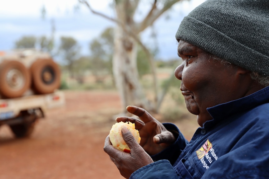 close up of female Indigenous ranger wearing a grey beanie and eating an orange.