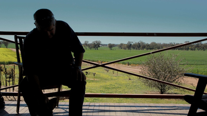 A man in silhouette sits on a veranda with farmland behind him