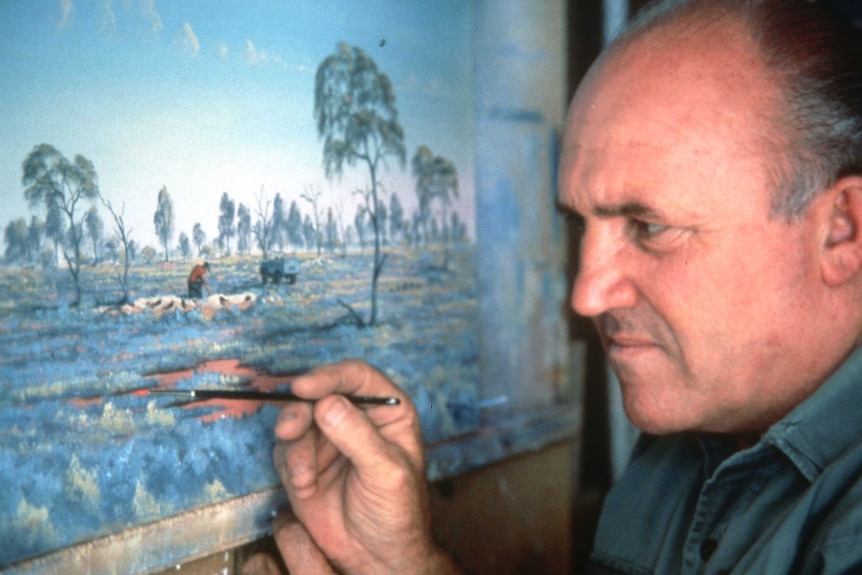 Up close of a man concentrating on painting a bush landscape with a fine brush.