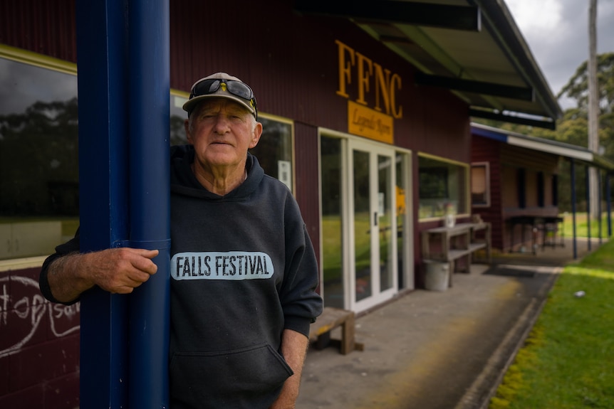 A man stands under the veranda of an old sports pavilion.  