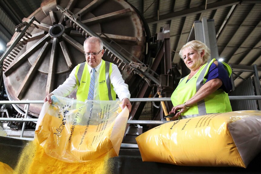 Scott Morrison pours a yellow powder into a tank as Michelle Landry stands alongside him in a factory