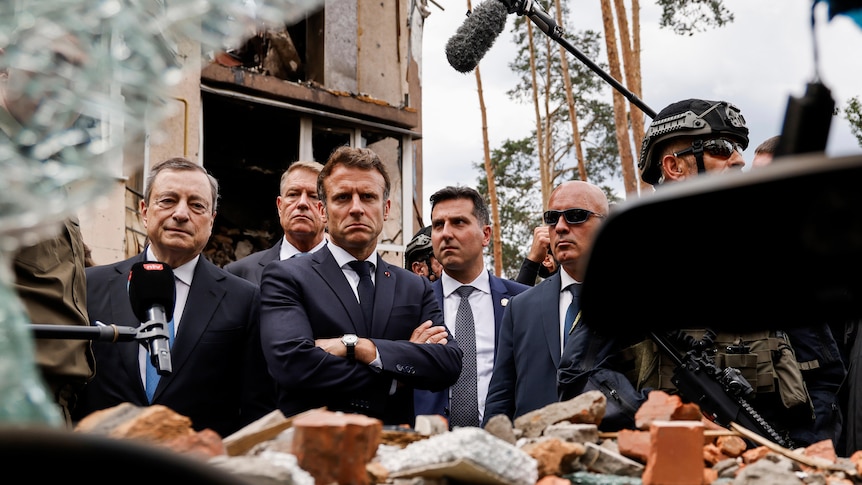 Men in suits look at destroyed remains of homes and cars.