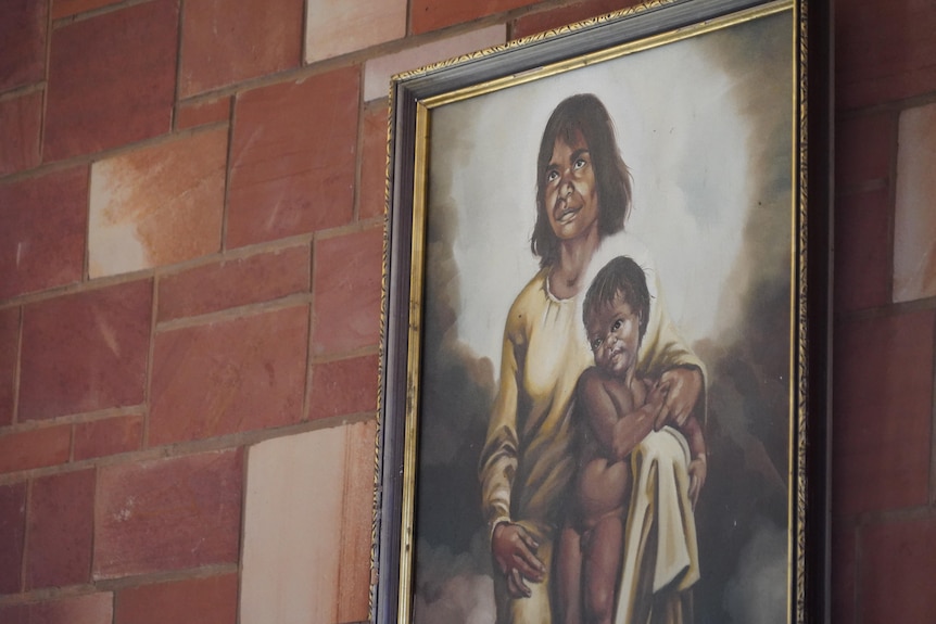 A picture of an Aboriginal Mary and Jesus against a red brick wall.