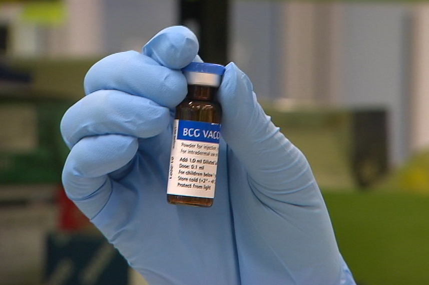 A person's hand with a blue glove on holding a brown bottle of BCG vaccine