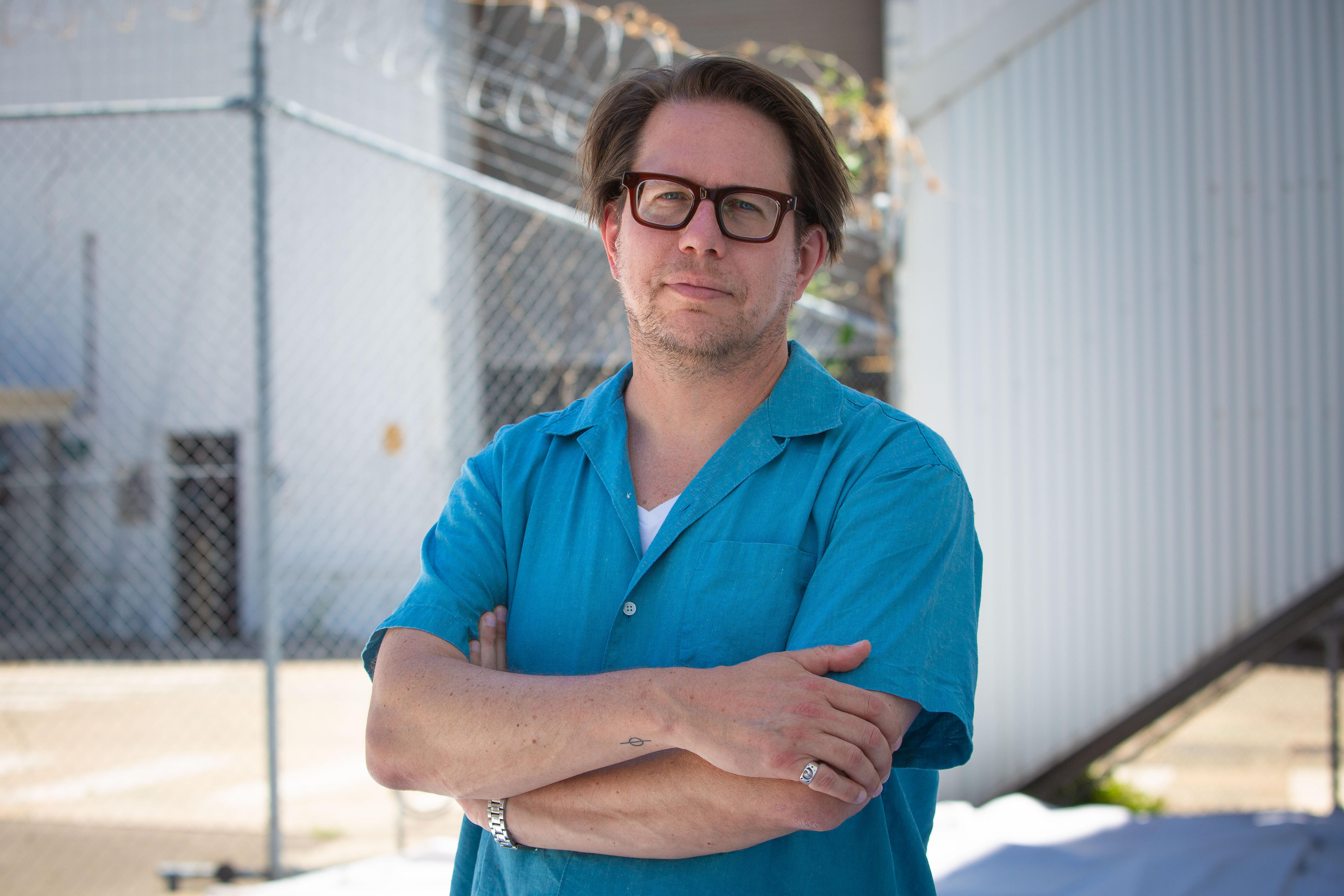 Um homem de óculos e camisa azul com os braços cruzados.