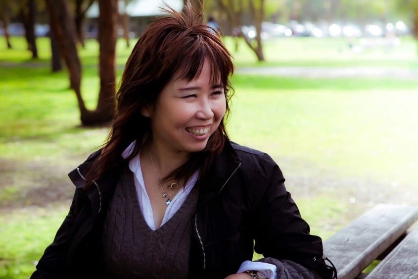 Bing Liu sits at a wooden park table, surrounded by green grass and trees.