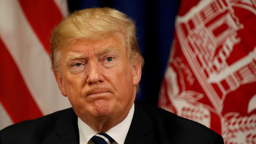 US President Donald Trump looks into the distance with his lips closed.