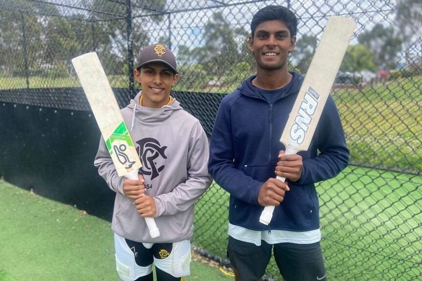 Two young men holding cricket bats while standing in the nets at training