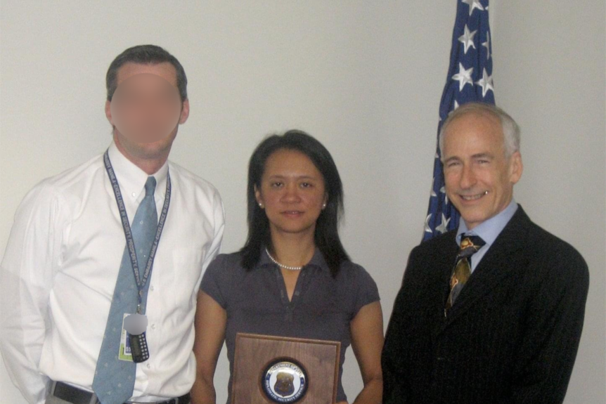 People wearing business attire pose for a photo holding an award in an office environment
