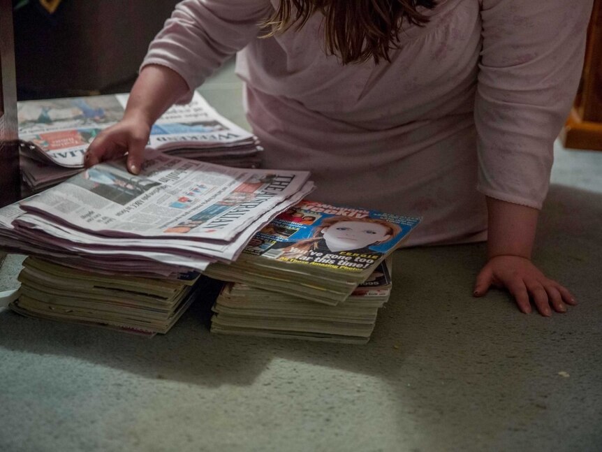 Kara sorts through magazines and copies of The Australian
