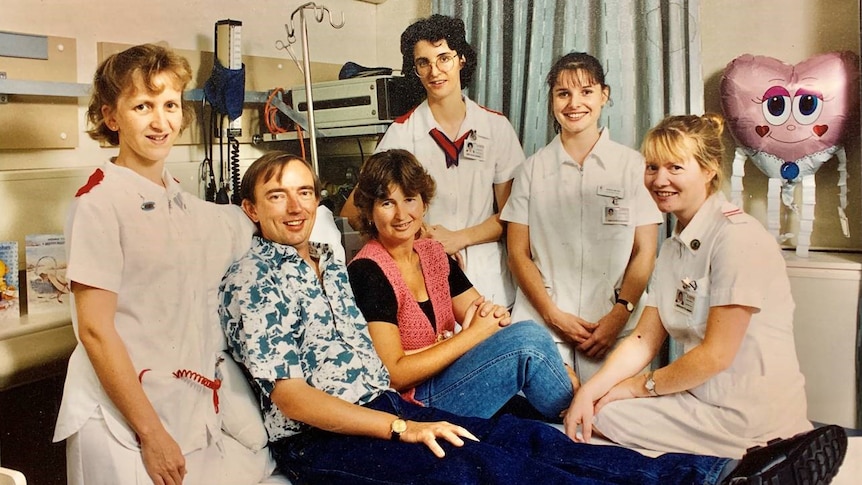 Rodney Western sitting on bed with wife, surrounded by four nursing staff  in the ICU