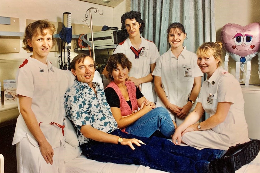 Rodney Western sitting on bed with wife, surrounded by four nursing staff  in the ICU
