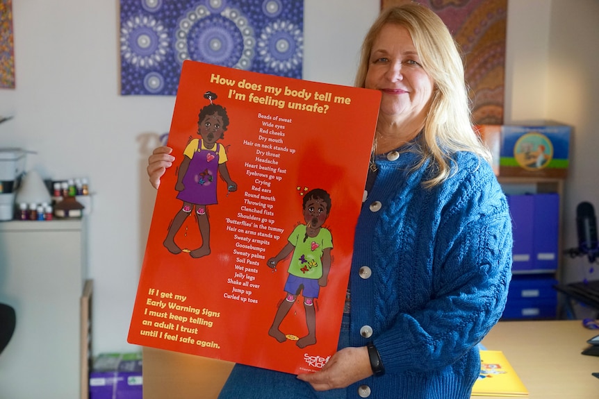 A smiling woman holds up a large poster