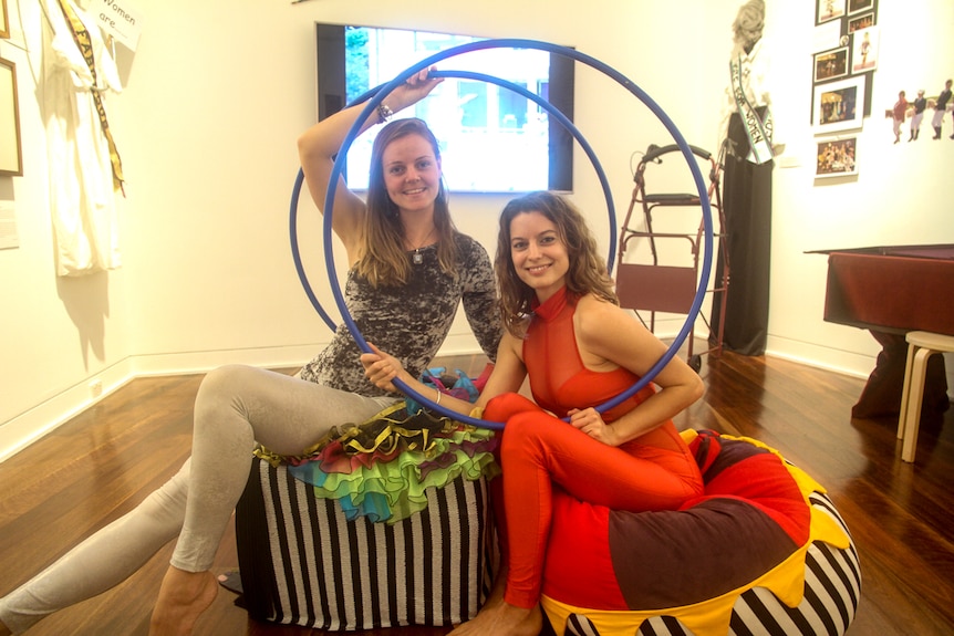 Two women sit with their hoops on a small stage
