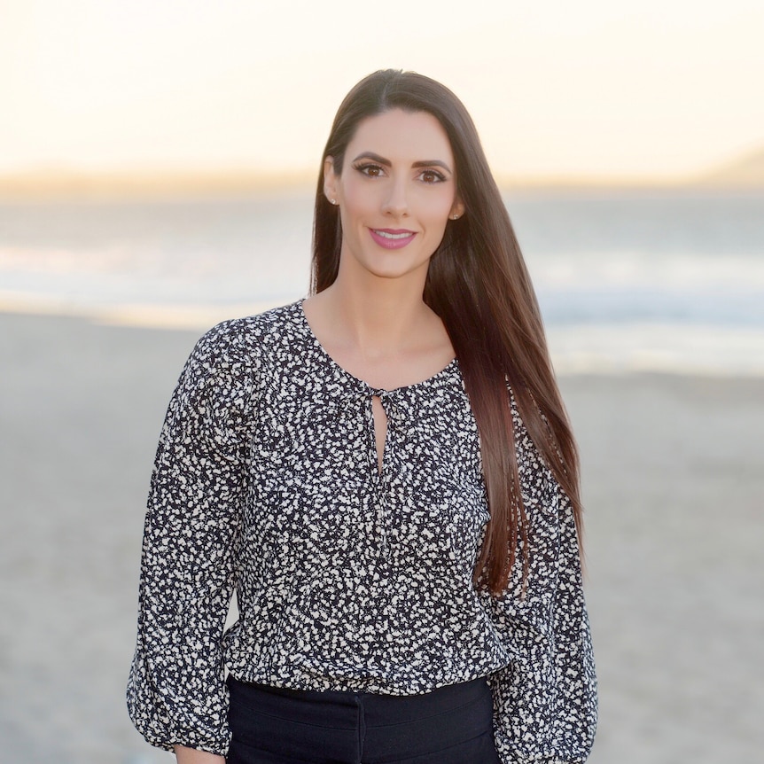 Woman in work blouse standing at the beach at sunset, gently smiling