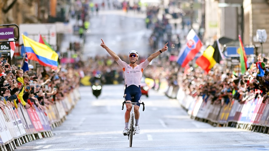 A cyclist raises his arms in triumph as he rolls across the line with crowds cheering at the end of a race.