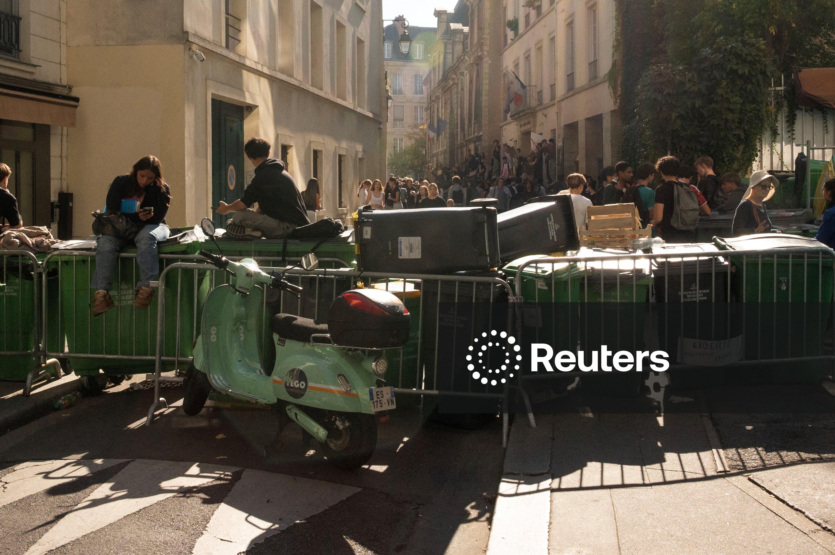 Crowds of students block a road off with rubbish bins, and protest outside a school.