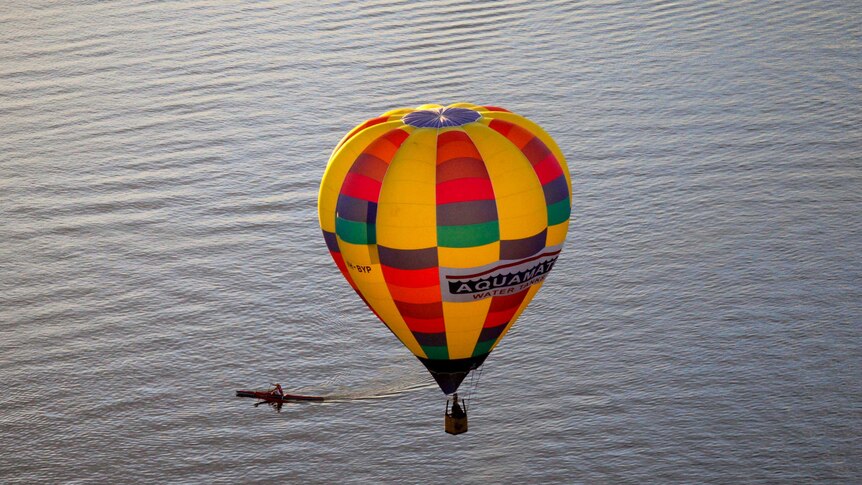 A hot air balloon flies over Lake Burley Griffin and a rowing boat.