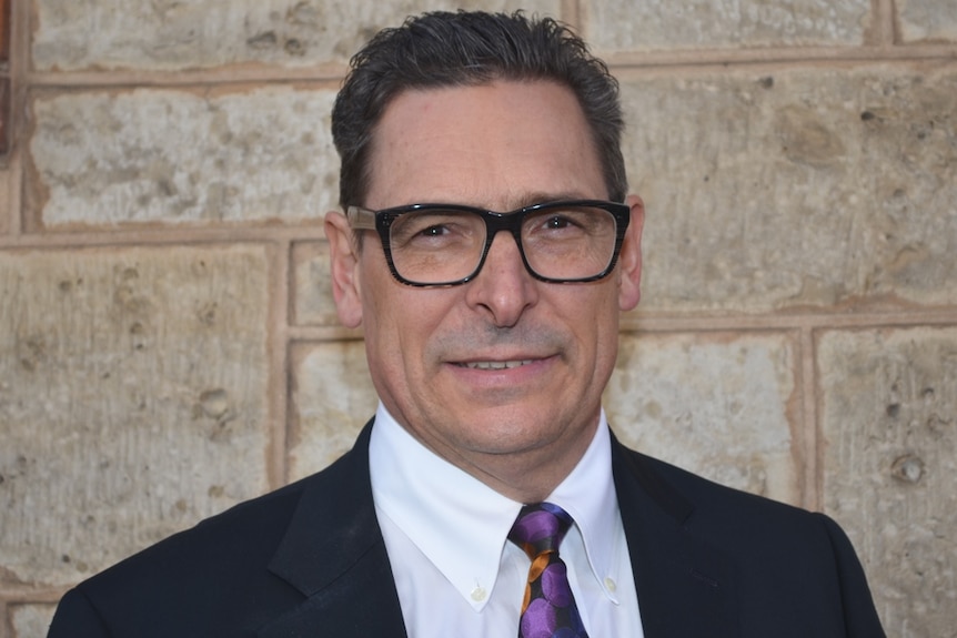 Headshot of Mark Chalmers standing against a sandstone wall