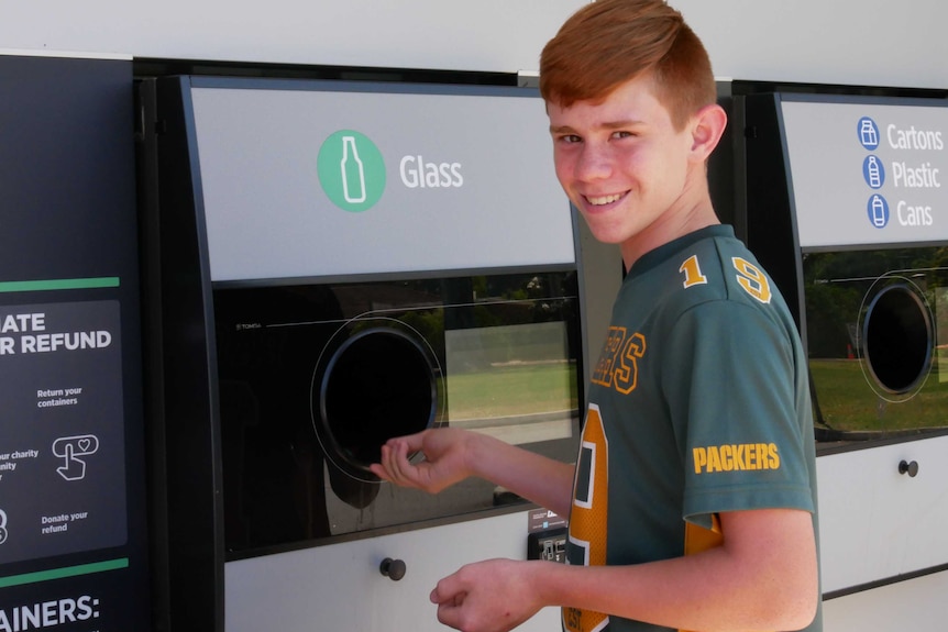 A young boy, around 13, smiling at the camera and depositing items into the return and earn chute.