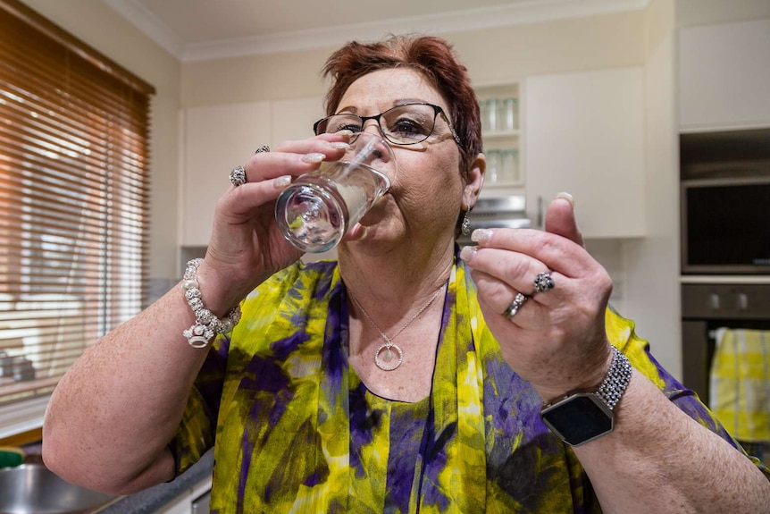 Wendy Benson drinking a glass of water after taking a tablet.