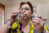 Wendy Benson drinking a glass of water after taking a tablet.