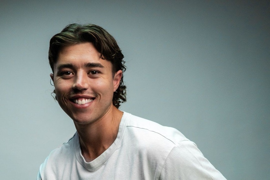 Bradley sits in a studio setting, smiling and wearing a white t-shirt.