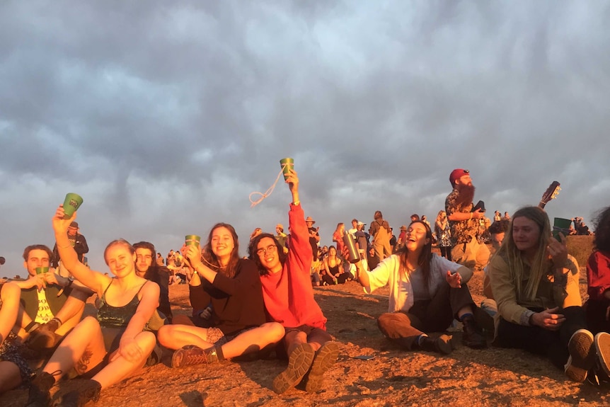A group of friends smile and sit on a hill at sunset.