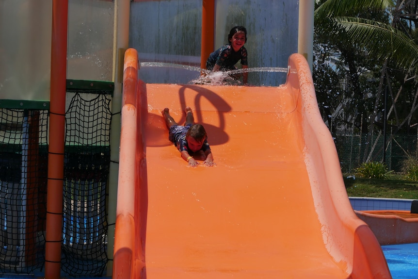 A little boy going down an orange slide with sprinklers
