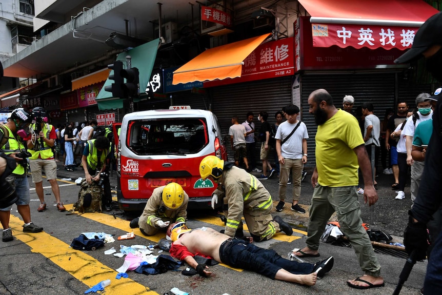 A bloodied taxi driver receives medical assistance from fire fighters as he lays on the street.