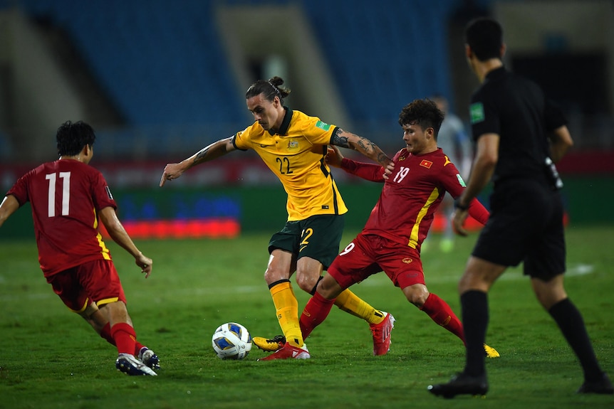 Jackson Irvine is surrounded by two Vietnamese opponents with the ball at his feet